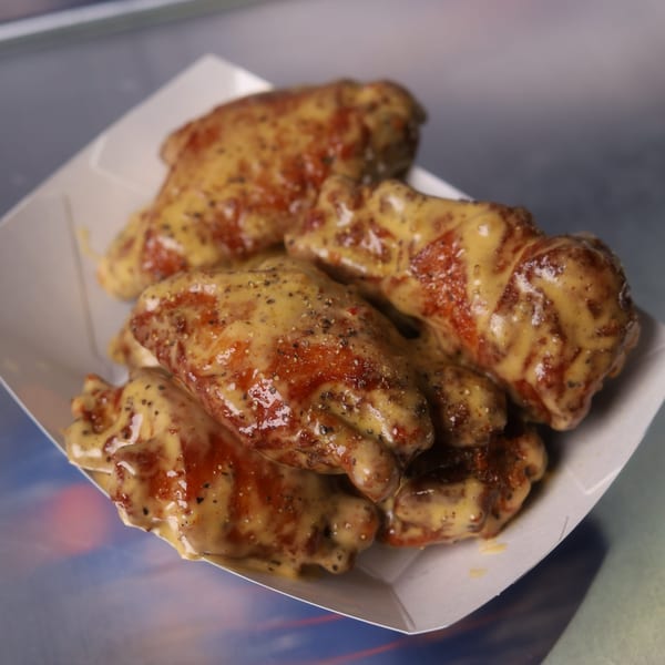 Astroid Burgers And Wings' chicken wings coated in a creamy sauce and black pepper, served in a paper tray.