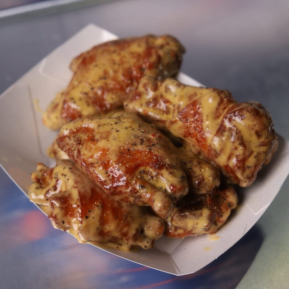 Astroid Burgers And Wings' chicken wings coated in a creamy sauce and black pepper, served in a paper tray.