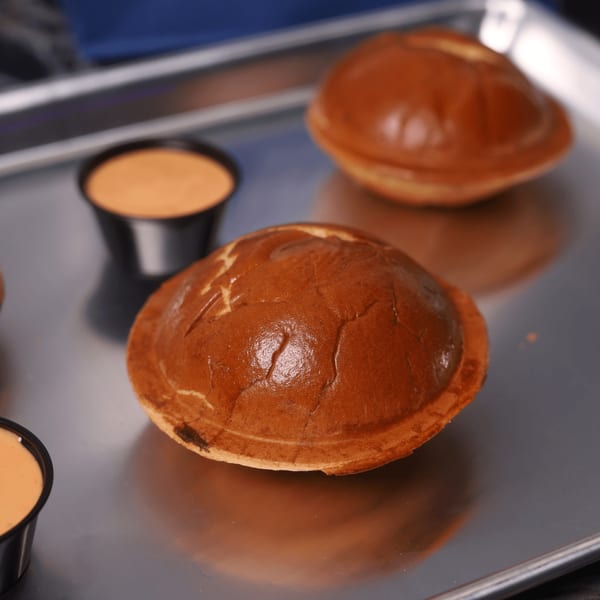 Two burger buns and two small cups of sauce on a metal tray at Astroid Burgers And Wings.