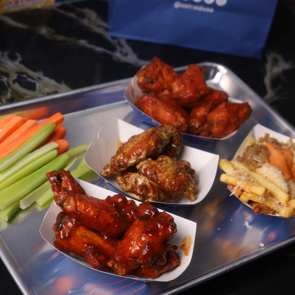 A tray with three servings of Astroid Burgers And Wings' chicken wings, fries, and vegetable sticks.
