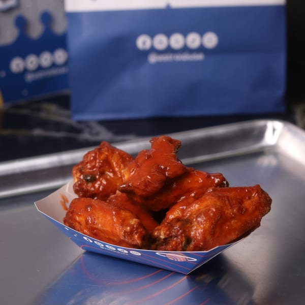 Astroid Burgers And Wings' buffalo wings in a branded paper tray on a metal surface.
