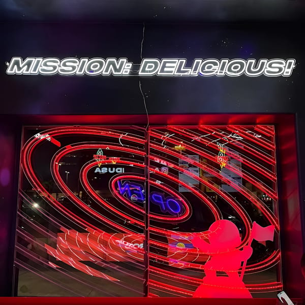 Astroid Burgers And Wings storefront with a "MISSION: DELICIOUS!" neon sign and red, swirling lights.