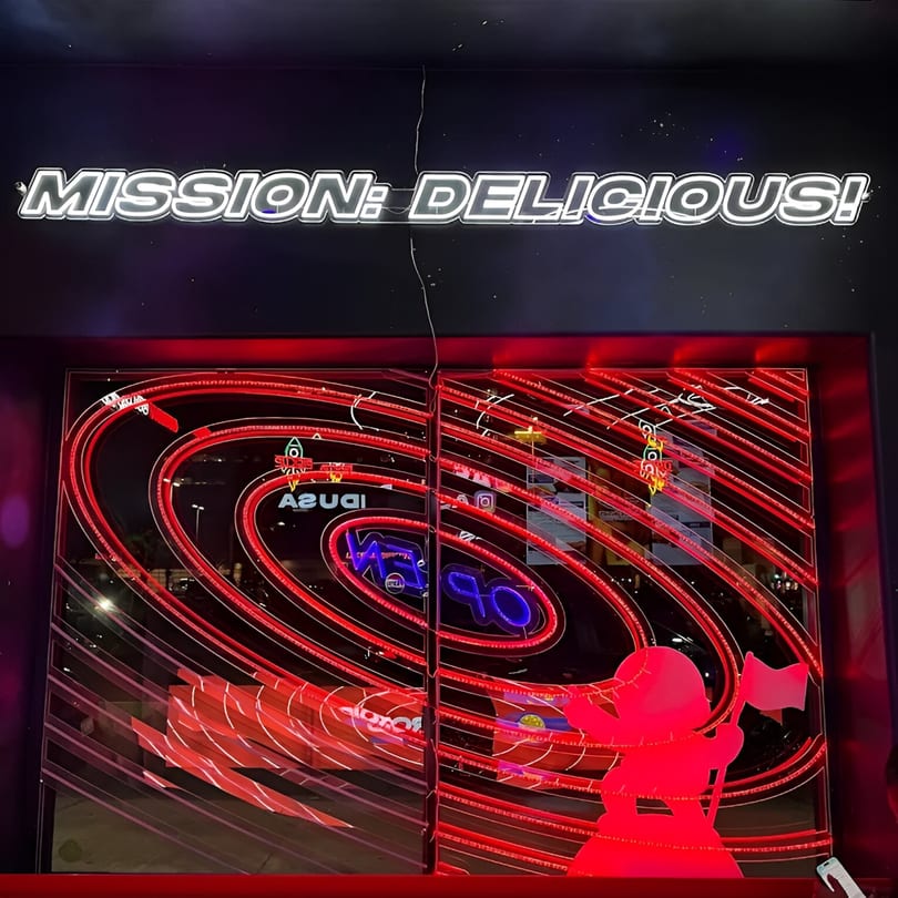 Astroid Burgers And Wings storefront with a "MISSION: DELICIOUS!" neon sign and red, swirling lights.