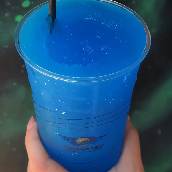 Hand holding a blue slushie drink with the Astroid Burgers And Wings logo on the cup.
