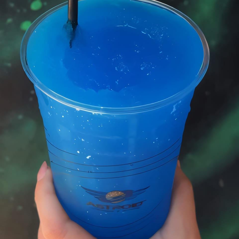 Hand holding a blue slushie drink with the Astroid Burgers And Wings logo on the cup.