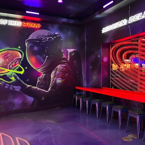 A neon-lit Astroid Burgers And Wings interior with a space-themed mural and bar seating.