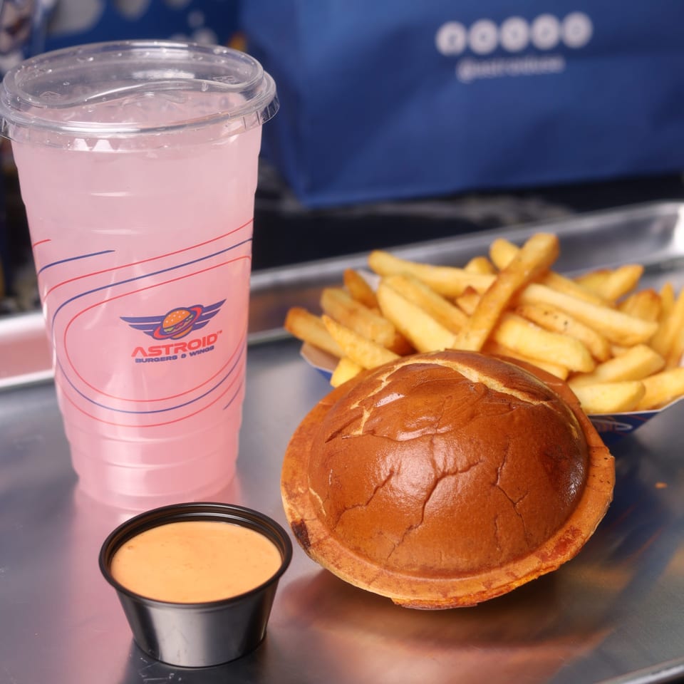 Astroid Burgers and Wings meal with a burger, fries, pink lemonade, and dipping sauce on a tray.
