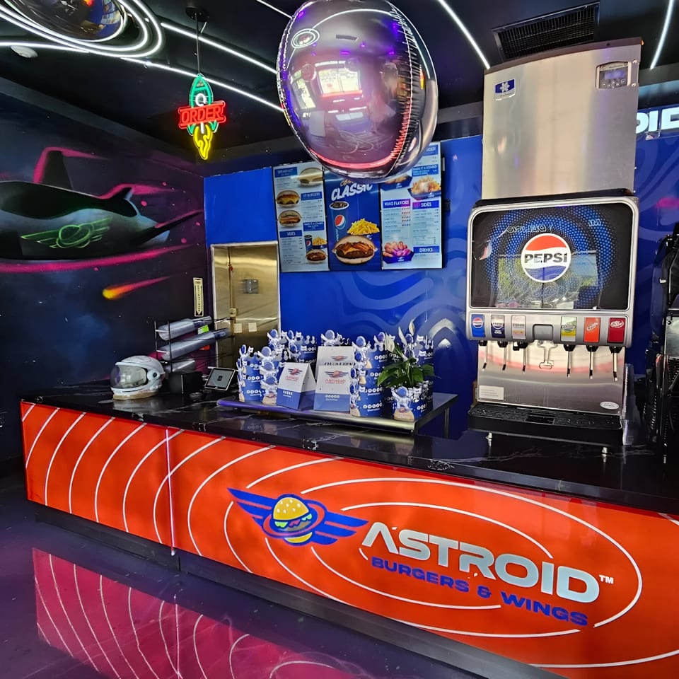 Astroid Burgers And Wings counter with space-themed decor, menu boards, and a Pepsi soda fountain.