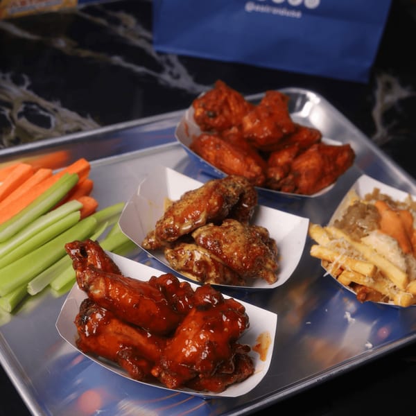 A tray of Astroid Burgers And Wings' buffalo wings, honey mustard wings, loaded fries, and vegetable sticks.